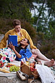 Weibliches Paar beim Picknick und beim Lesen eines Buches