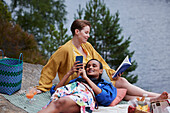 Weibliches Paar macht Picknick, liest ein Buch und telefoniert