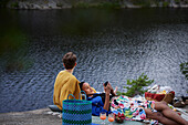 Female couple having picnic by river and using phone