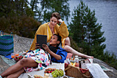 Weibliches Paar picknickt am Fluss und benutzt ein Tablet