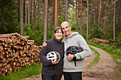 Portrait of smiling couple holding bike helmets in forest