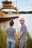 Senior couple holding hands and looking at industrial barge