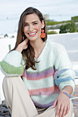 Young woman in light-coloured knitted jumper with coloured stripes and beige trousers