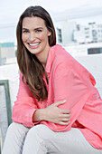 Young woman in salmon coloured shirt with pearl necklace and light coloured trousers