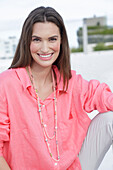 Young woman in salmon coloured shirt with pearl necklace and light coloured trousers