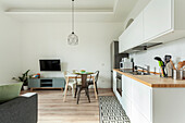 Weiße Küchenzeile mit Holzarbeitsplatte und kleiner Essbereich im Wohnzimmer