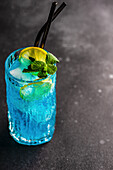 Cocktail high glass with blue kamikaze drink decorated with fresh mint and slice of lemon