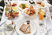 Breakfast table with scrambled eggs, croissants, pastries, waffles, cheese, sausage, coffee and fruit juice