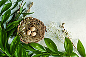 Osternest mit Eiern, daneben Gypsophila und Blätterzweige auf Betonuntergrund