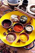 Various spices in small bowls on a yellow plate