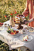 Table with cake, bouquet and berries in the middle of a field