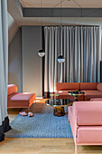 Rosa Sofa mit eleganten, schwarzen Beistelltischen und stilvollen Leuchten in offenem Wohnraum
