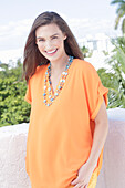 A cheerful young woman wearing an orange summer blouse with a necklace