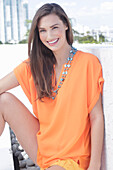 A cheerful young woman wearing an orange summer blouse with a necklace