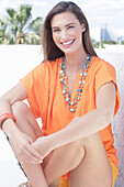 A cheerful young woman wearing an orange summer blouse with a necklace