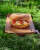 Sesame bagel with sardines and tomatoes on a wooden board in the grass