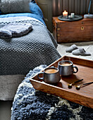 Doppelbett mit grauer Tagesdecke, im Vordergrund Holztablett mit Kaffeetassen