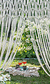 View through macramé curtain to picnic blanket with drinks in the garden