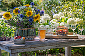 Sommerlicher Blumenstrauß mit Sonnenblumen und Kugeldisteln auf Holztisch im Garten