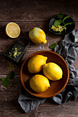 Lemons in a wooden bowl, next to them zest grater and mint leaves