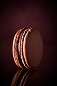 Schokoladen-Macaron vor braunem Hintergrund (Close Up)