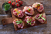 Canapes with ham, salami, asparagus and tomatoes on a board