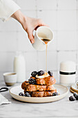 Pouring maple syrup on Challah toast with yogurt and blackberries