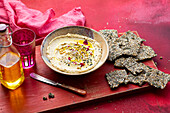 Hummus mit Schwarzkümmel, Pinienkernen, Essblüten und Saaten-Cracker