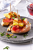 Baguette slices topped with Serrano ham, egg and caramelized onions
