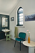 Badezimmer mit Bogenglasfenster, Waschbecken, Stuhl und dekorativen Blumen