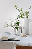 Gedeckter Frühlingstisch mit verschiedenen weißen Vasen, Wilder Möhre, Arabischer Sternblume, Gräser, Efeu und Heidelbeerzweig