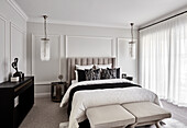 Opulent bedroom in neutral tones with paneled walls and hanging chandeliers