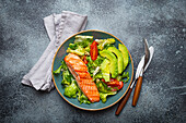 A grilled salmon steak and vegetable salad with avocado