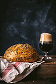 Round bread poppyseed loaf with dark foamy beer in glass