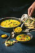 Curried yellow lentils in a large bowl spooned into a serving bowl with naan bread