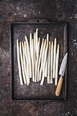 Fresh white asparagus spears with knife on a rustic baking tray