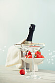 A bottle of champagne, two glasses and strawberries in a bowl