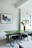 Dining table with green table top, black chairs, flowers and picture