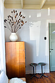 Wooden cabinet with dried flowers in vase, stool and green door