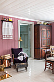 Old wooden cupboard and upholstered armchair with woollen blanket in country-style room