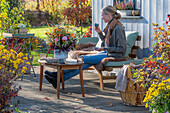 Frau auf herbstlicher Terrasse mit Blumendekoration beim Kaffeetrinken