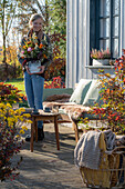 Frau trägt herbstlichen Blumenstrauss mit Zinnien (Zinnia), Rosen, Herbstastern auf der Terrasse