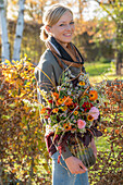 Frau trägt herbstlichen Blumenstrauss unter dem Arm mit Zinnien (Zinnia), Ringelblumen (Calendula), Fuchsschwanz (Amaranthus caudatus), Rosen, Herbstastern