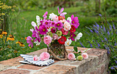 Blumenstrauß aus Cosmea (Cosmos), Zinnien (Zinnia), Rosen 'Double Delight' (Rosa) auf Gartenmauer, Sonnenhut (Echinacea) im Blumenbeet