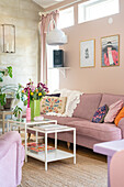 Pink sofa and patterned cushions in living room with flowers and plant