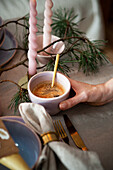 Tasse Kaffee in Hand auf gedecktem Tisch mit Tannenzweigen und Kerzen