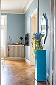 Blue plinth with bouquet of flowers, wooden floor and light blue walls