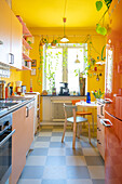 Orangefarbener Kühlschrank und rosa Schränke in Küche mit gelben Wänden