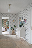 Hallway with white chest of drawers, picture gallery and round rugs on wooden floor