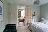 Green daybed and white bed in a bedroom with a view into the living room